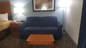 Una camera d'albergo con un divano blu, un comodino in legno con una lampada, un telefono e un quadro incorniciato appeso al muro.