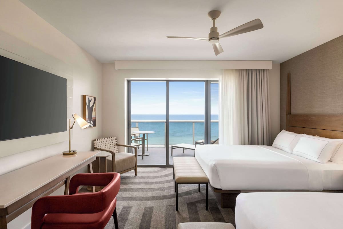 A hotel room with a bed, a desk, a chair, a bench, and a view of the ocean.