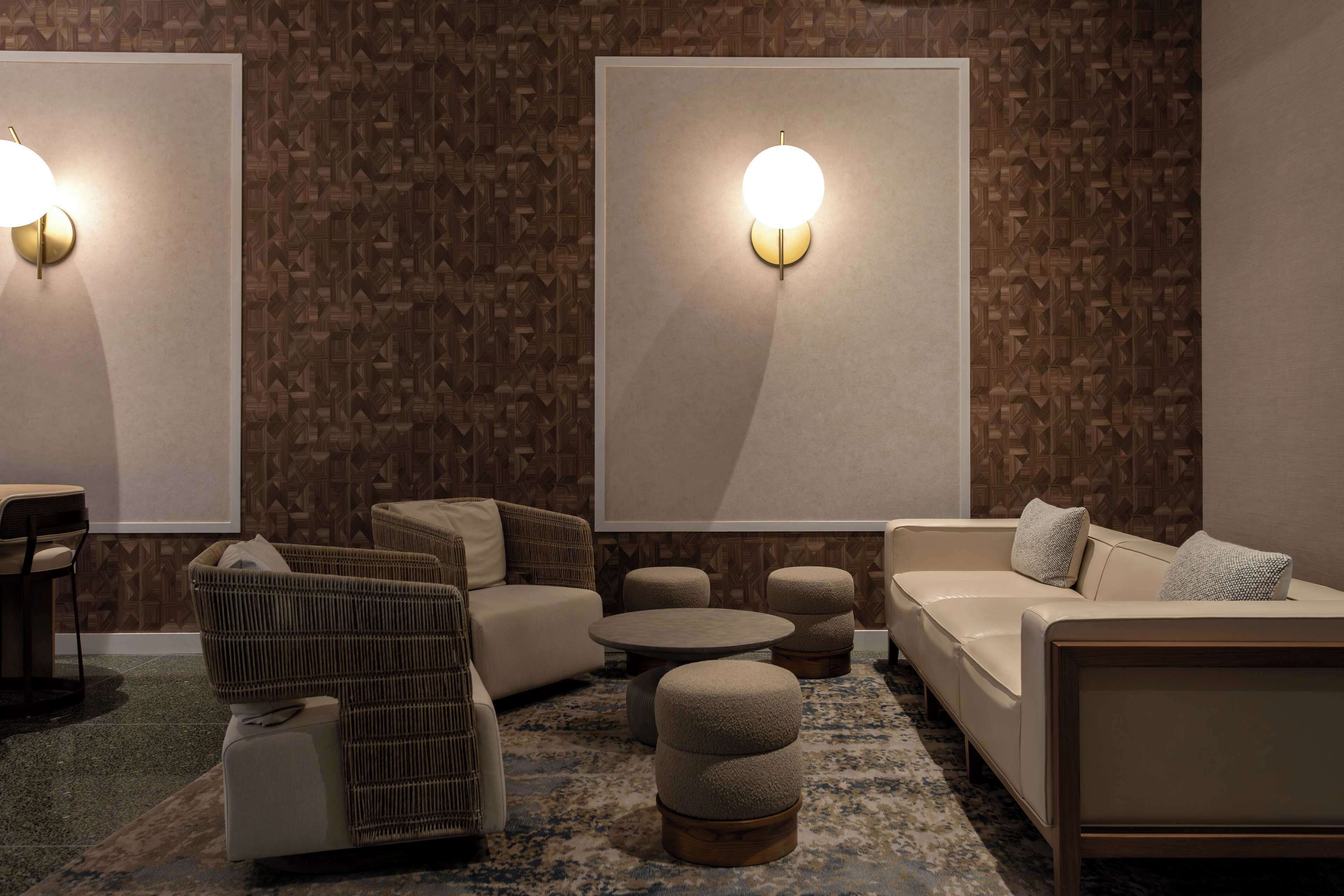 A modern lounge area with a patterned wall, a sofa, a chair, ottomans, and a round coffee table.