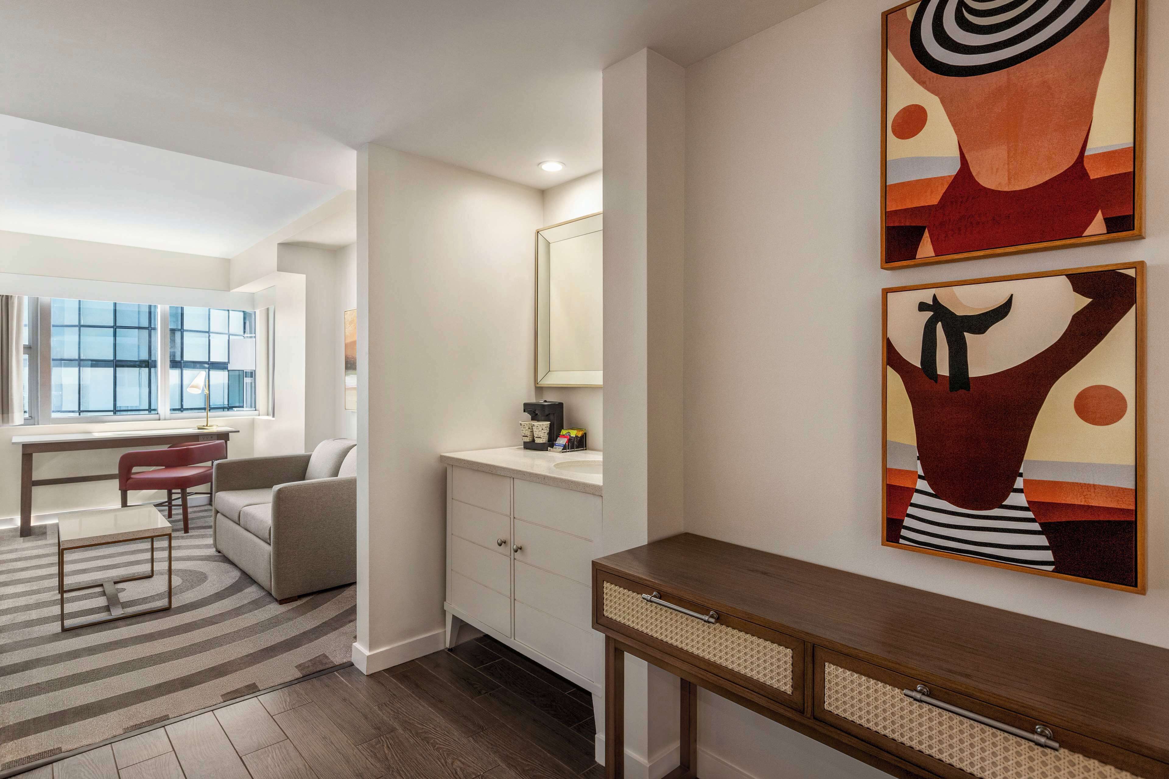 Un salon moderne avec un canapé, une table basse et un bureau. Une fenêtre offre une vue sur l’extérieur.
