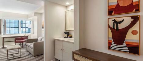 Un salon moderne avec un canapé, une table basse et un bureau. Une fenêtre offre une vue sur l’extérieur.