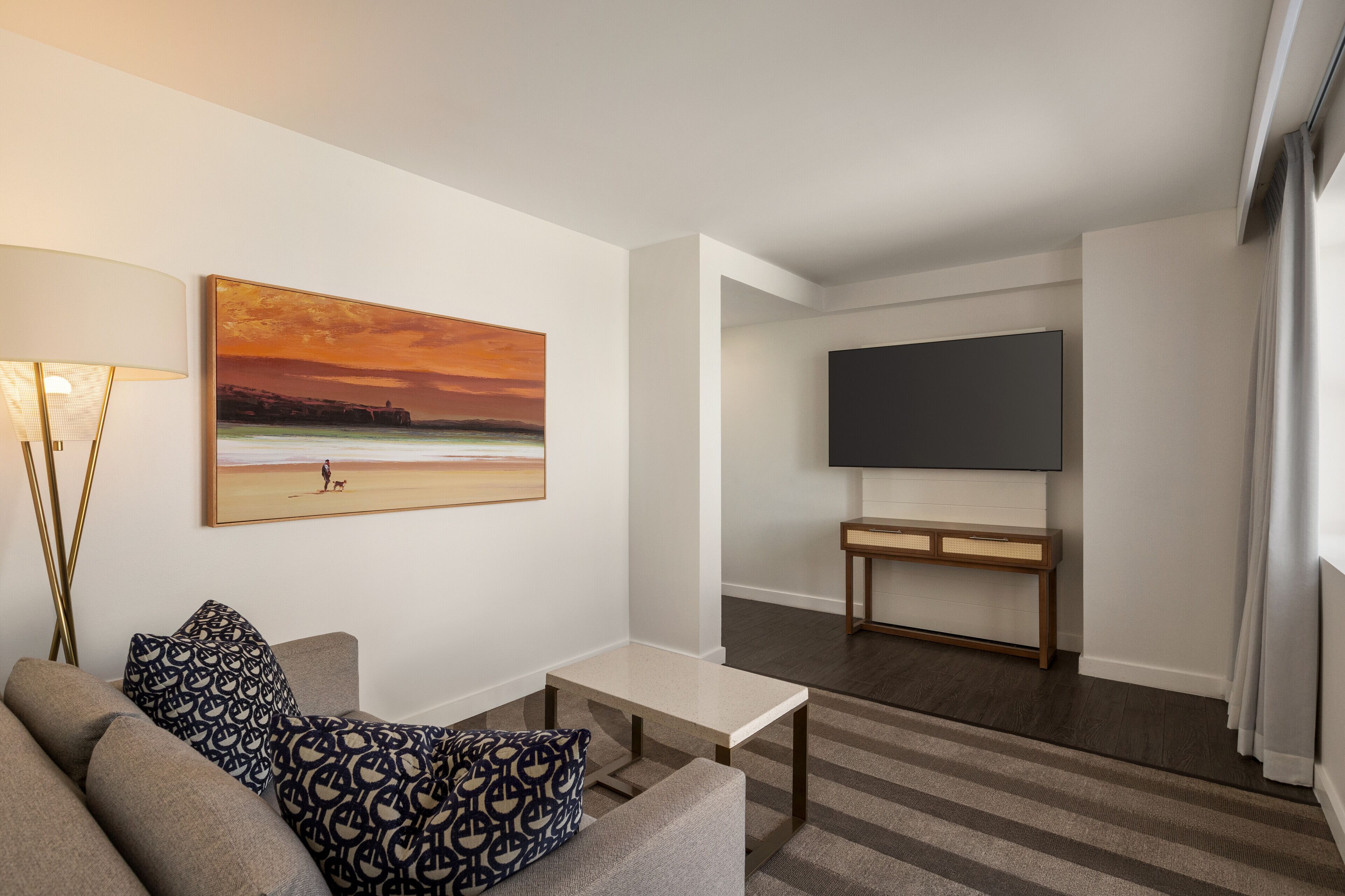 Una sala de estar moderna con un sofá, una mesa de centro, un cuadro, un televisor de pantalla plana y una consola.