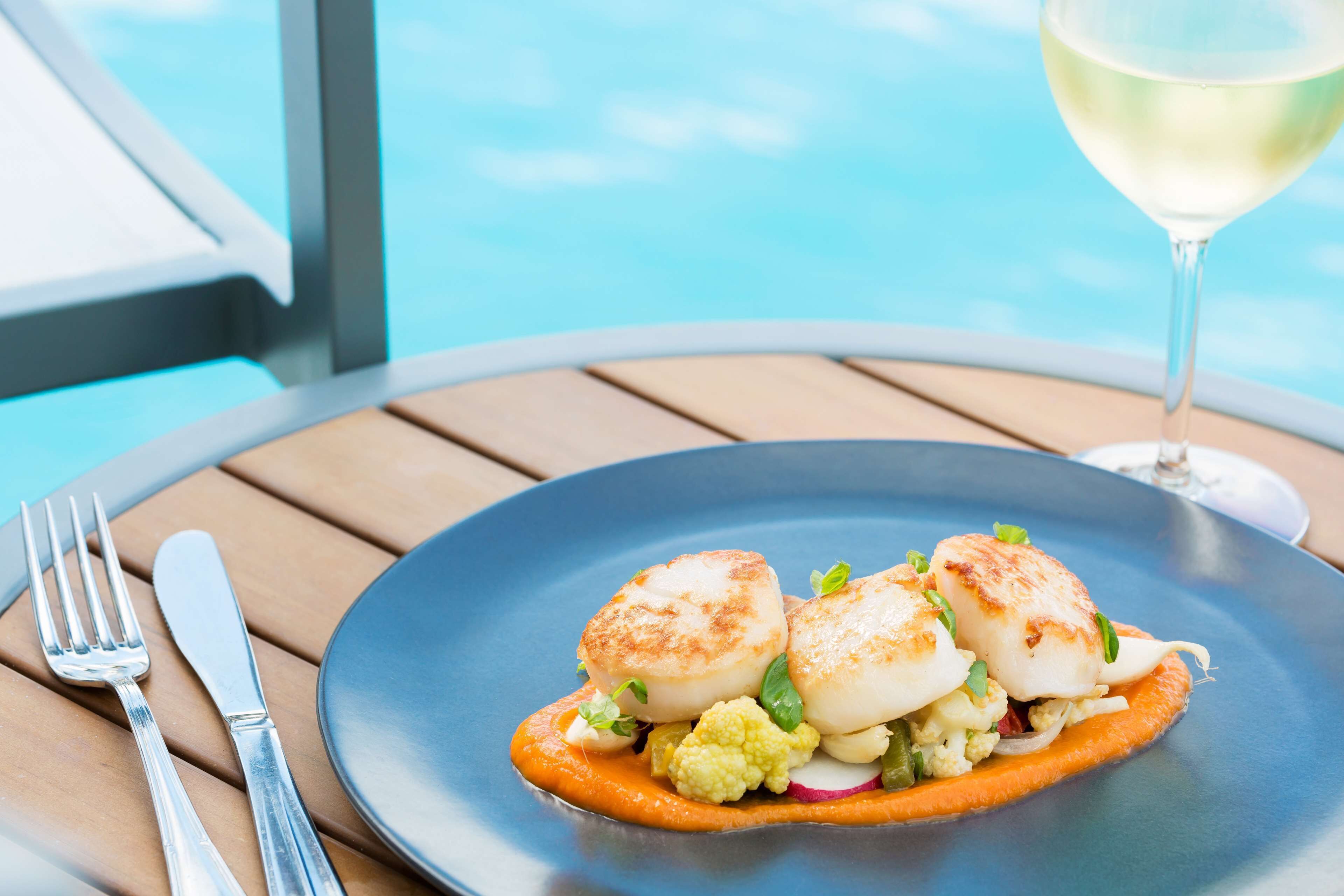 A plate of food with a fork and knife on a table by a poolside.