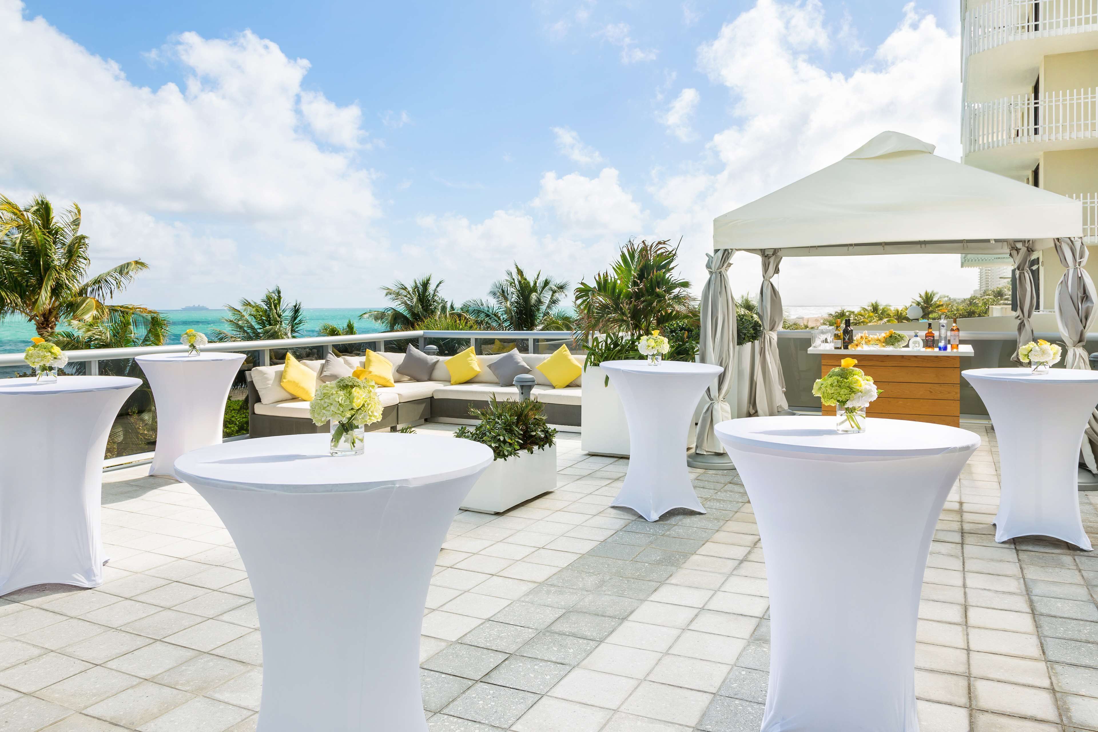A rooftop terrace with white tables, a sofa with yellow cushions, and a white canopy.