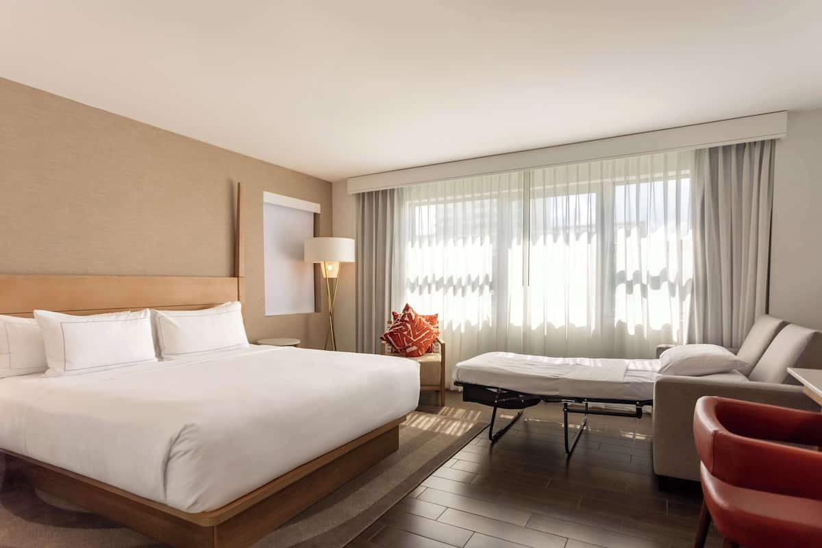 A hotel room with a large bed, a sofa, a small table, and a window with curtains.