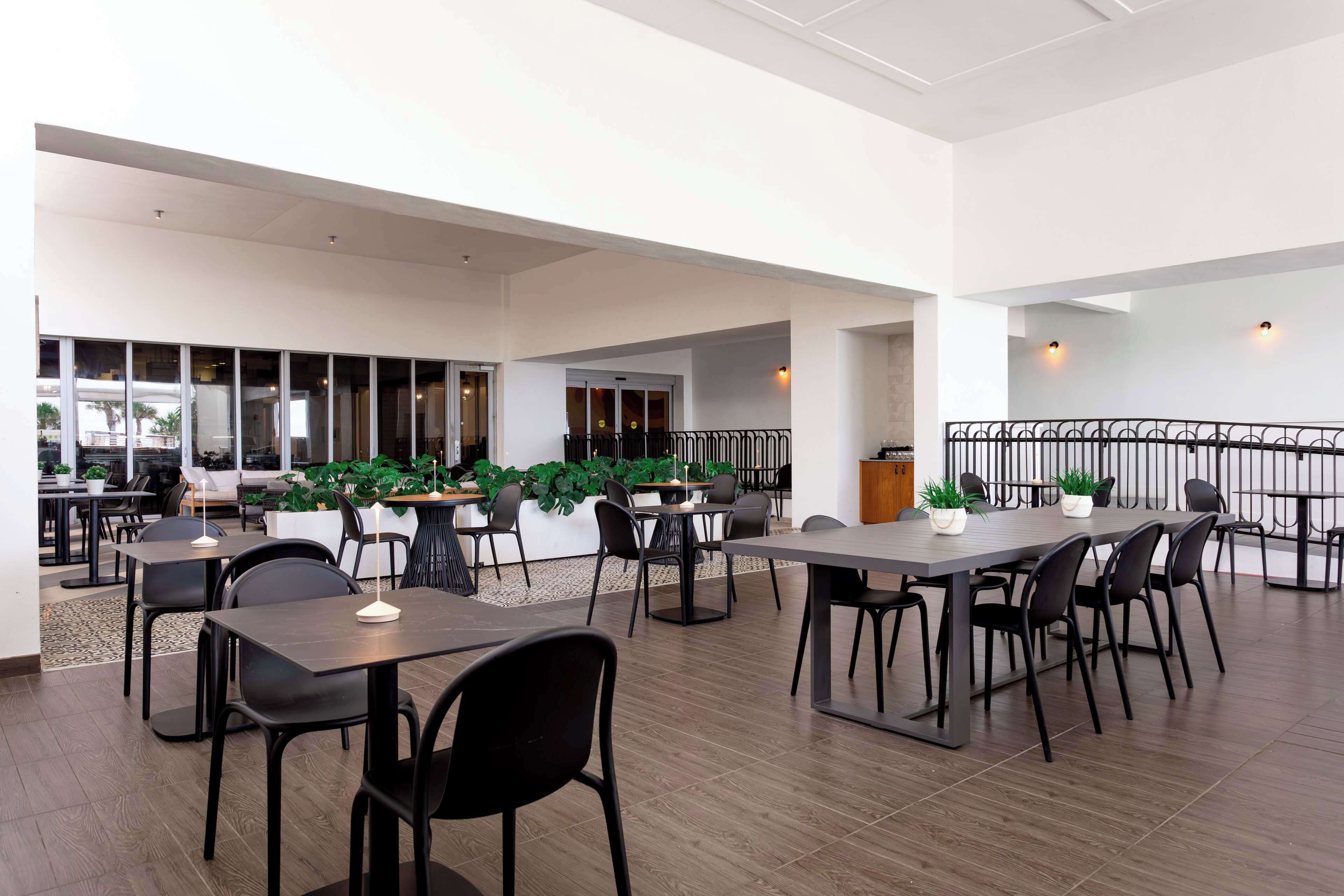 A spacious indoor area with multiple tables and chairs, a balcony with a railing, and potted plants.