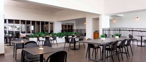 A spacious indoor area with multiple tables and chairs, a balcony with a railing, and potted plants.