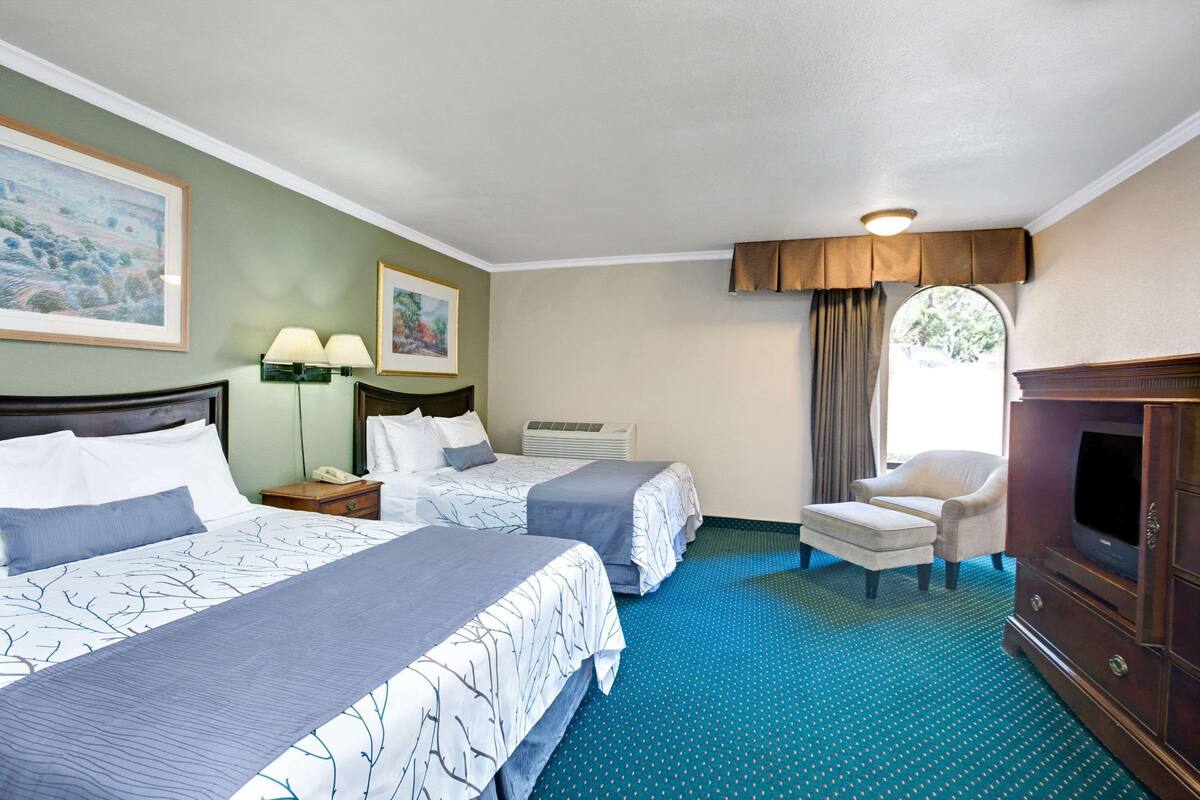 A hotel room with two beds, a chair, a TV, and a window with curtains.