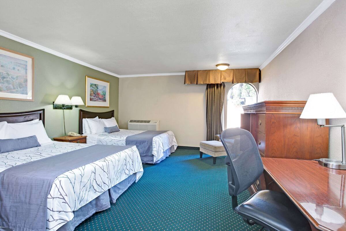 A hotel room with two beds, a desk, a chair, a lamp, a telephone, and a window with curtains.