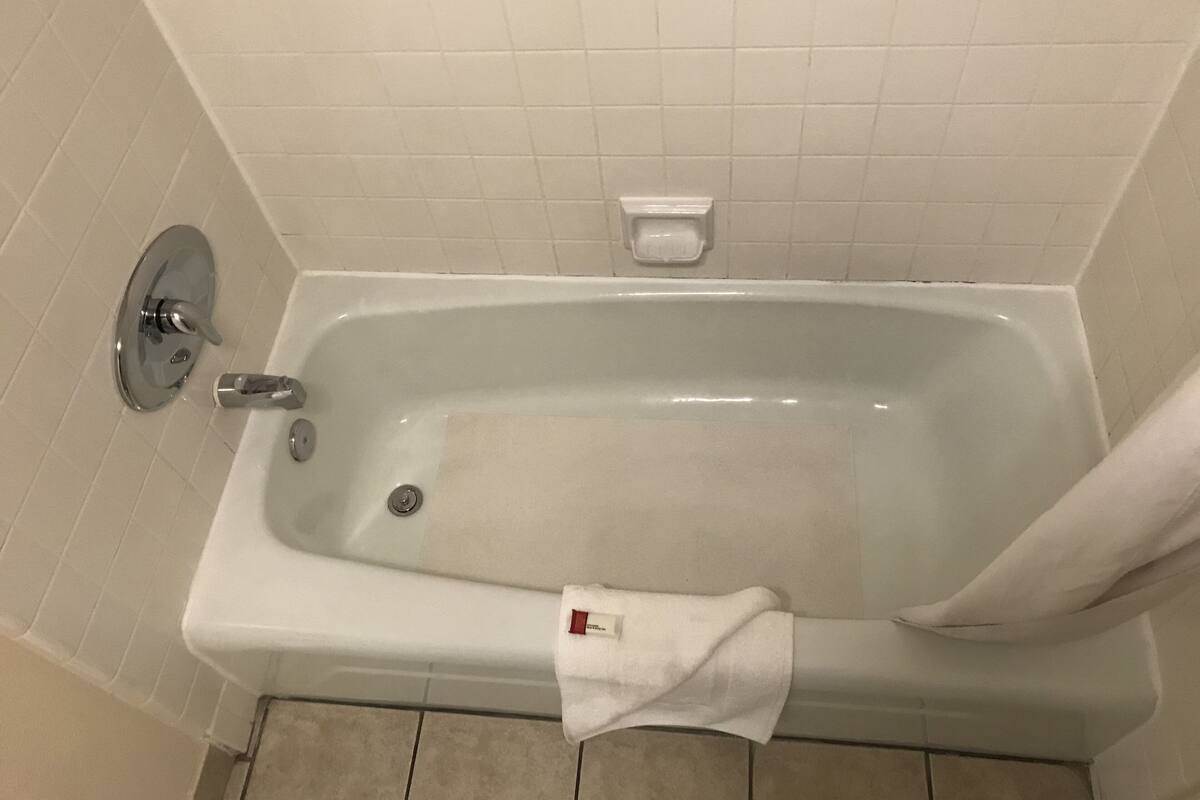 A standard white bathtub with a faucet and a soap dish on the wall.