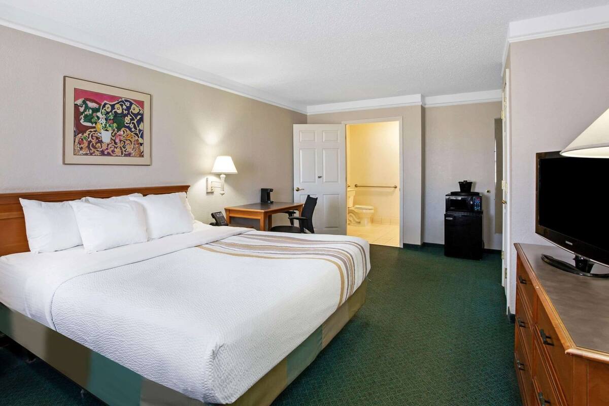 Habitación de hotel con una cama grande, un escritorio, un televisor, una cafetera y la puerta del baño.