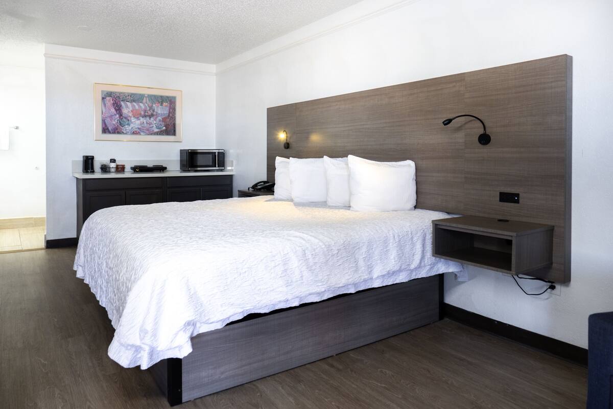 Una habitación de hotel moderna con una cama grande, una mesita de noche, un televisor montado y un cuadro en la pared.