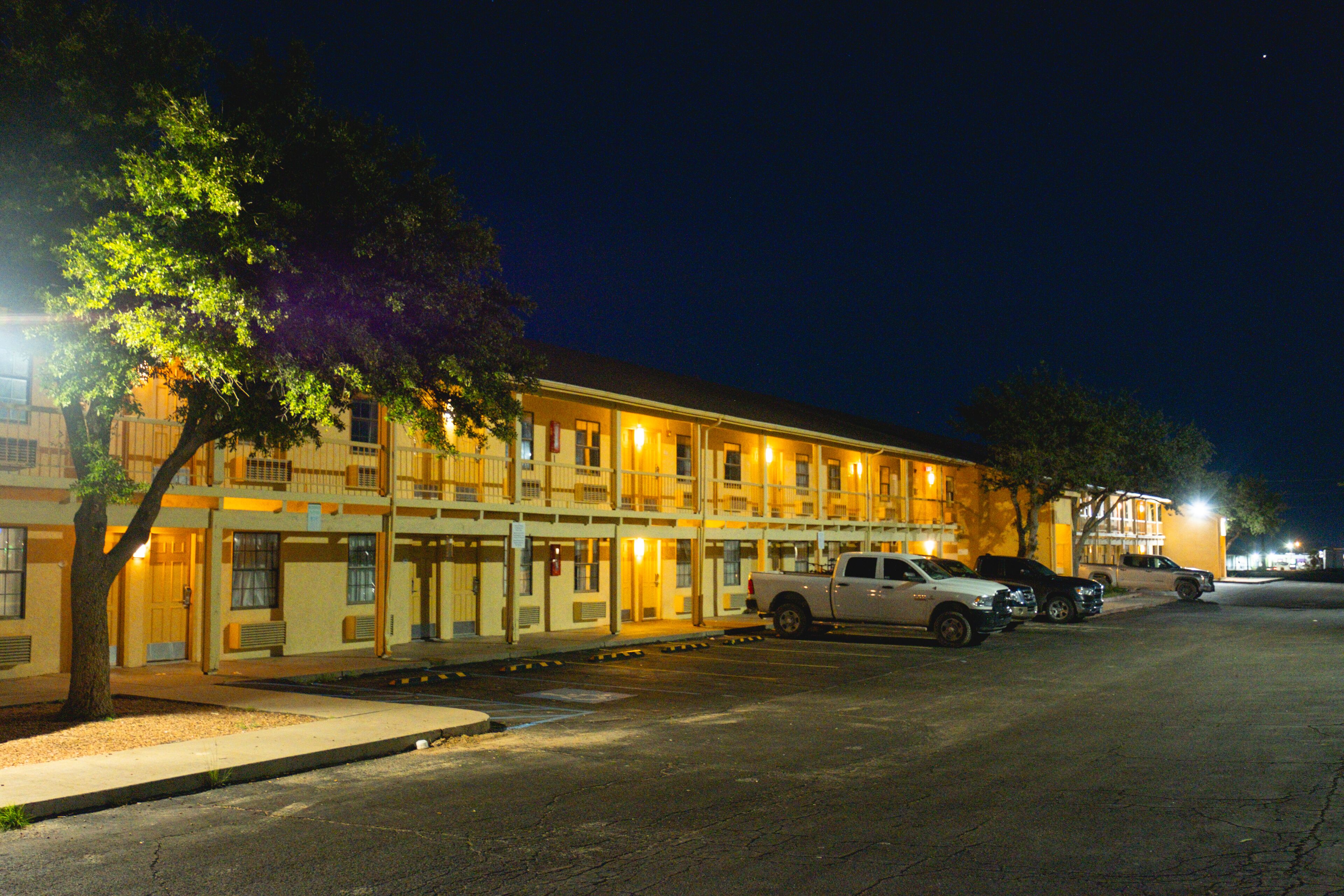 A motel with multiple floors, a parking lot, and a tree in front.