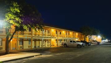 A motel with multiple floors, a parking lot, and a tree in front.