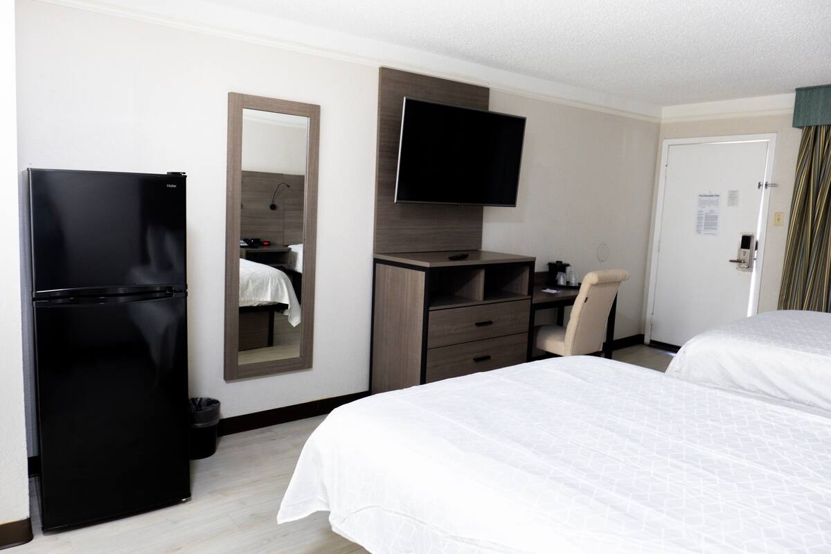 Una habitación de hotel con cama, escritorio, silla, televisor y refrigerador.