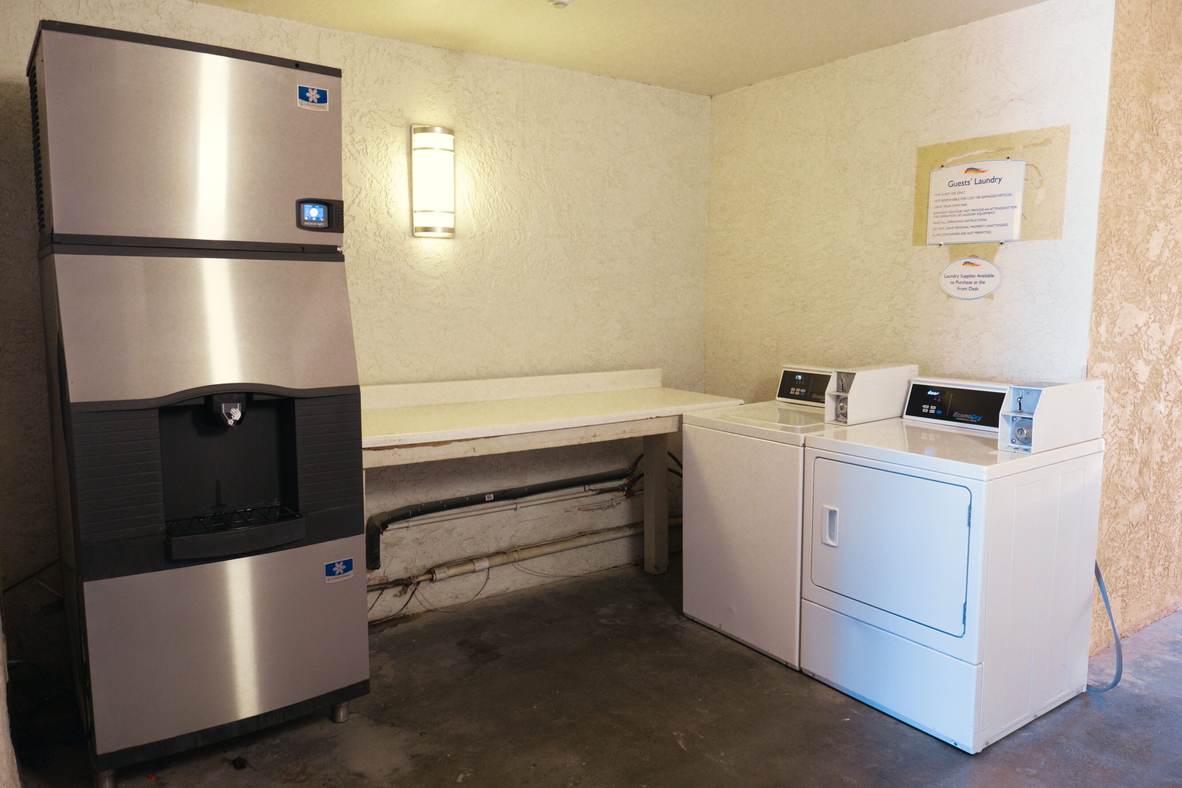 A compact kitchenette with a stainless steel refrigerator, a water dispenser, a microwave, and a washing machine.