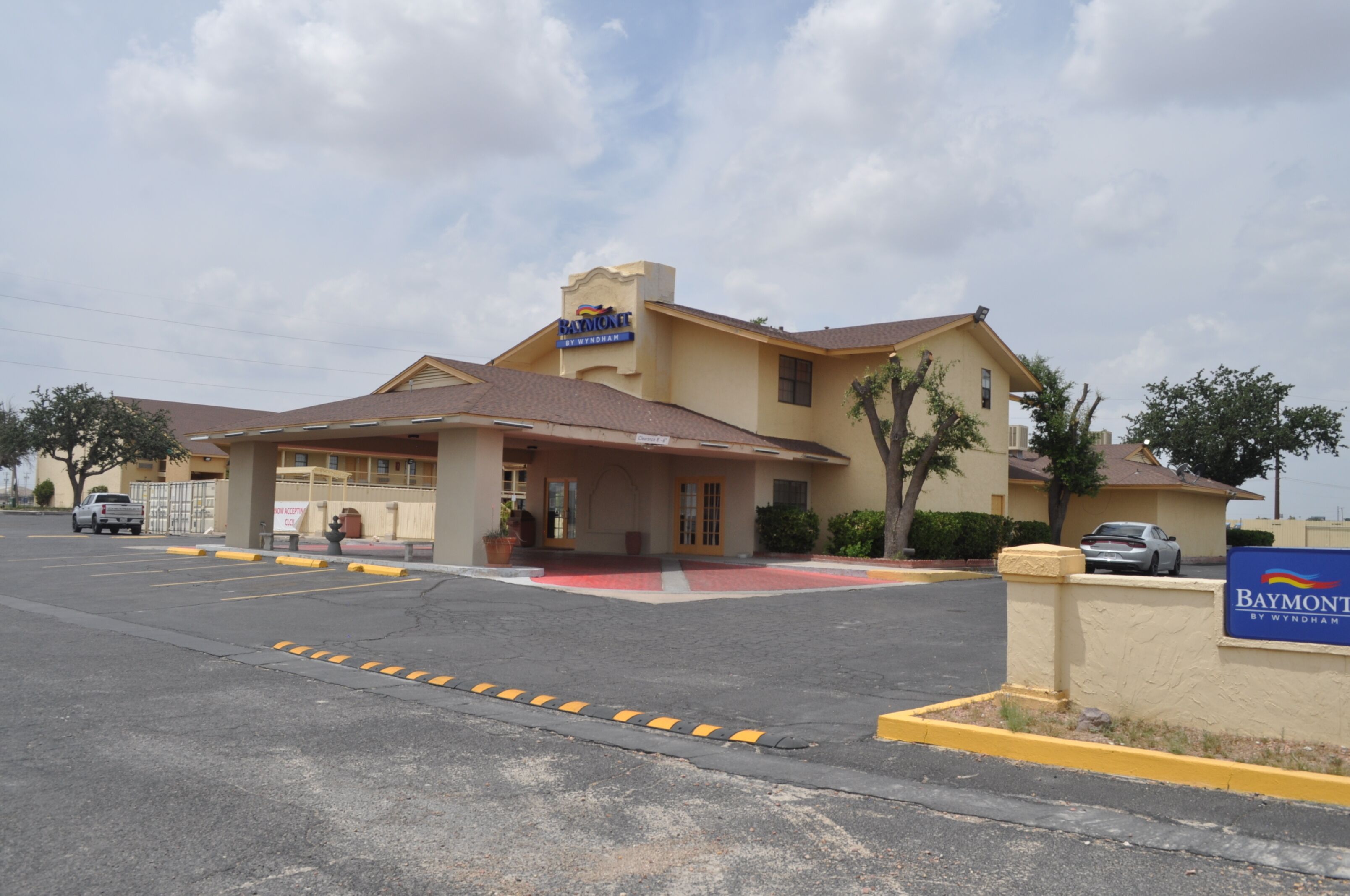 A hotel with a yellow facade, a covered entrance, and a parking lot.