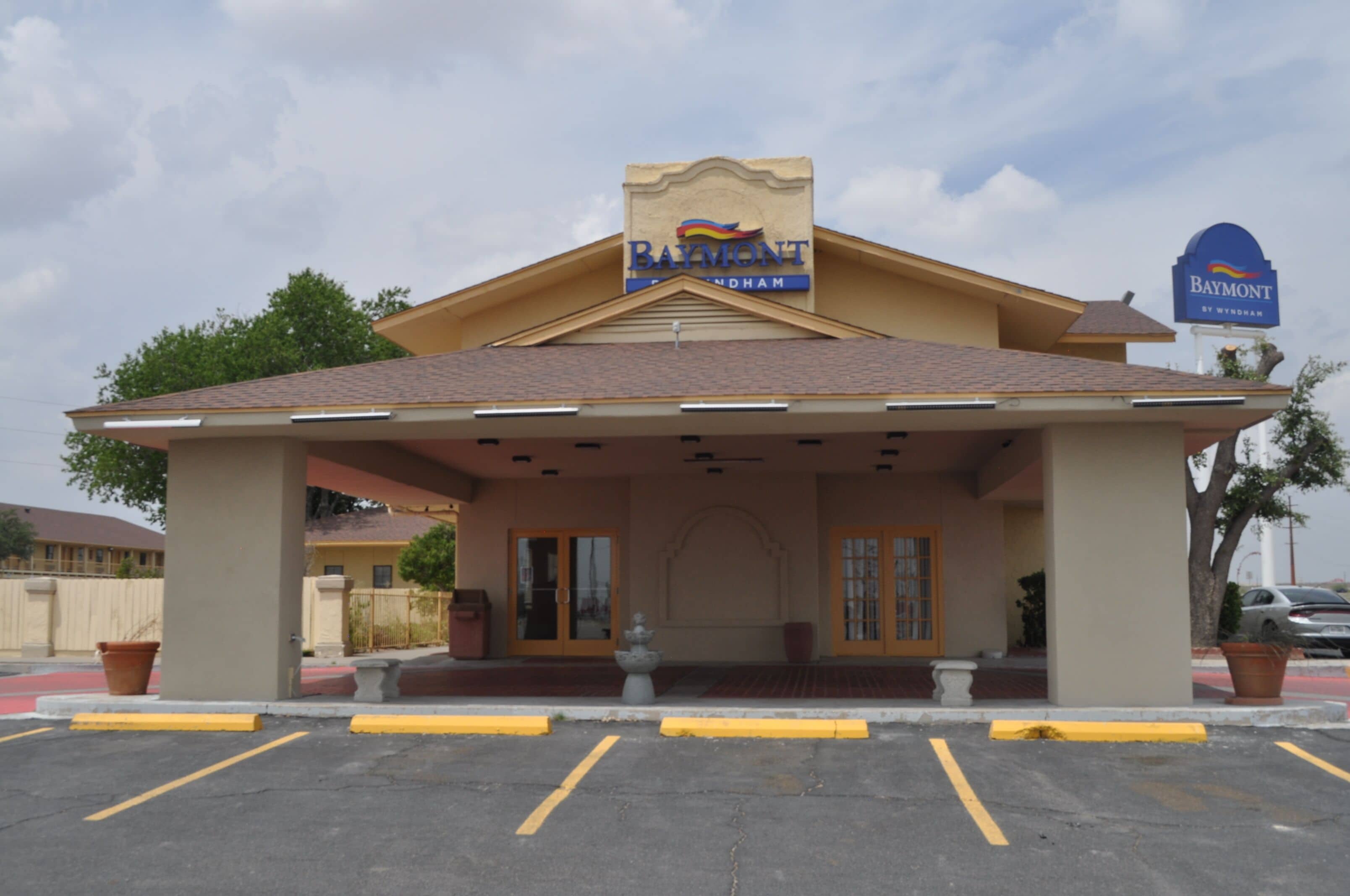 A hotel with a covered entrance, a signboard, and a parking lot.