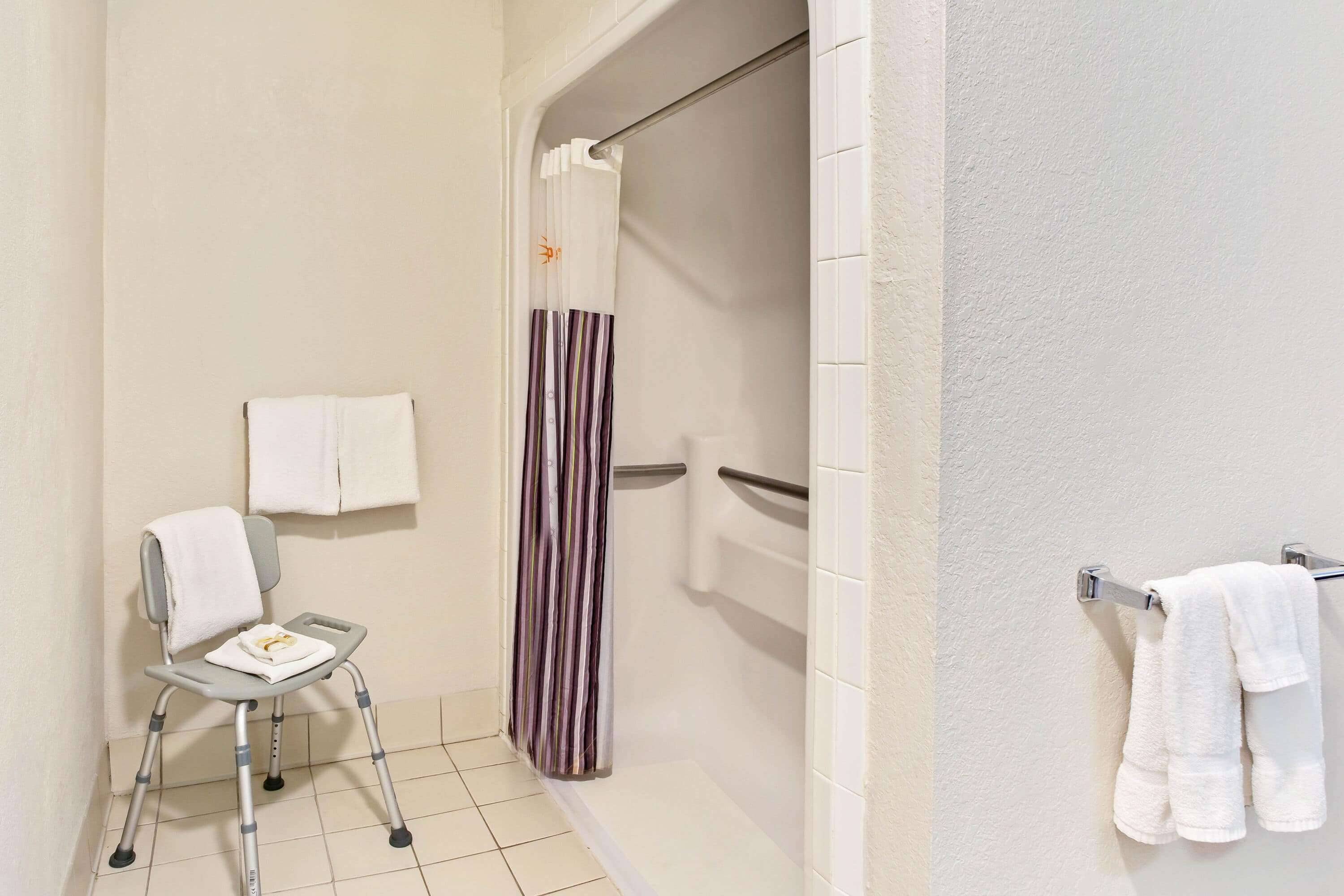 Un baño con ducha, inodoro y una silla con toalla.