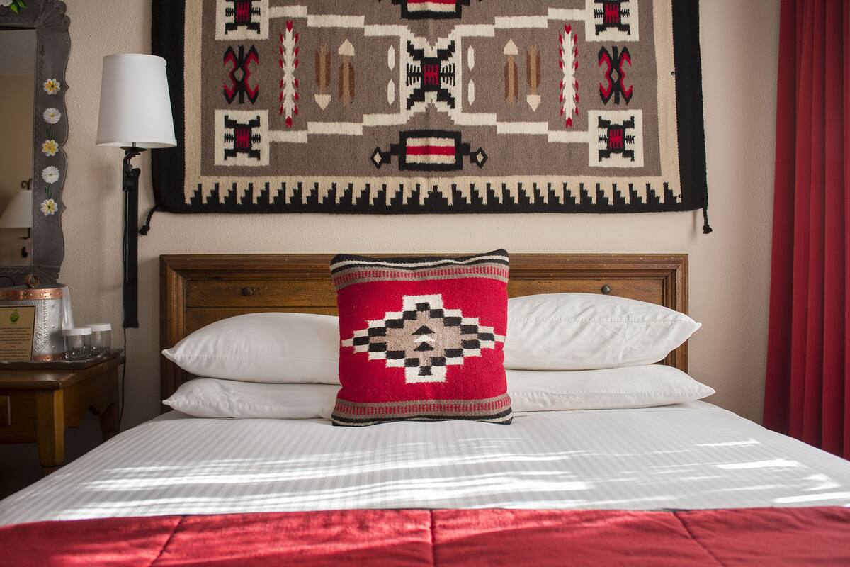 A neatly made bed with white linens, a red throw blanket, and a decorative pillow with a geometric pattern.