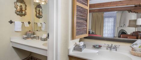 A bathroom with a white sink, wooden vanity, and a large mirror. There are towels on the wall and a small shelf with toiletries.