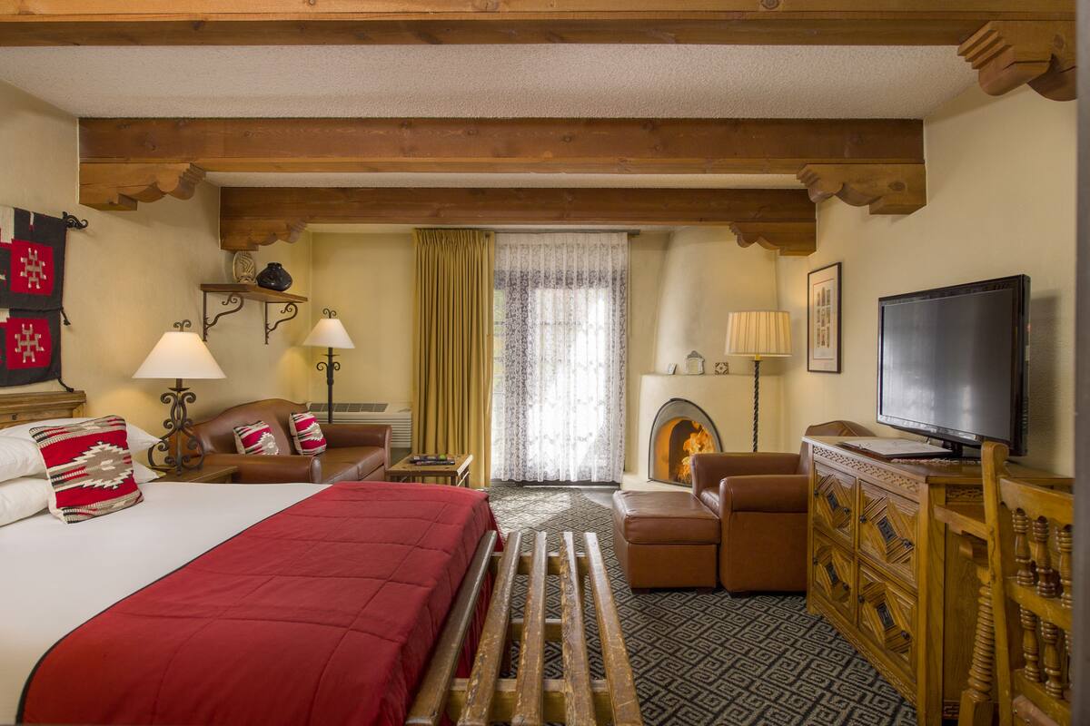 A hotel room with a bed, a television, a fireplace, and a wooden bench.