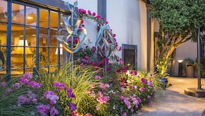 A building with large windows, a metal sculpture, and a garden with pink flowers.