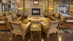 A cozy living room with a brick fireplace, leather sofas, a wooden coffee table, and a large window providing natural light.