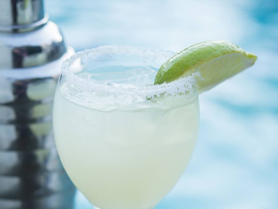 A cocktail glass with a lime garnish, a shaker, and a blurred background.
