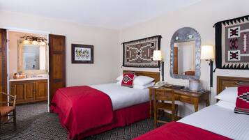 A hotel room with two beds, a wooden desk, a chair, a mirror, a framed picture, and a patterned rug.