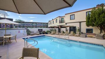 A pool area with lounge chairs, umbrellas, and a building with a balcony in the background.