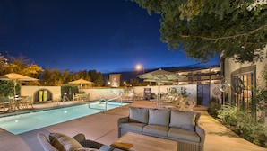 An outdoor pool area with lounge chairs, a sofa, and umbrellas.