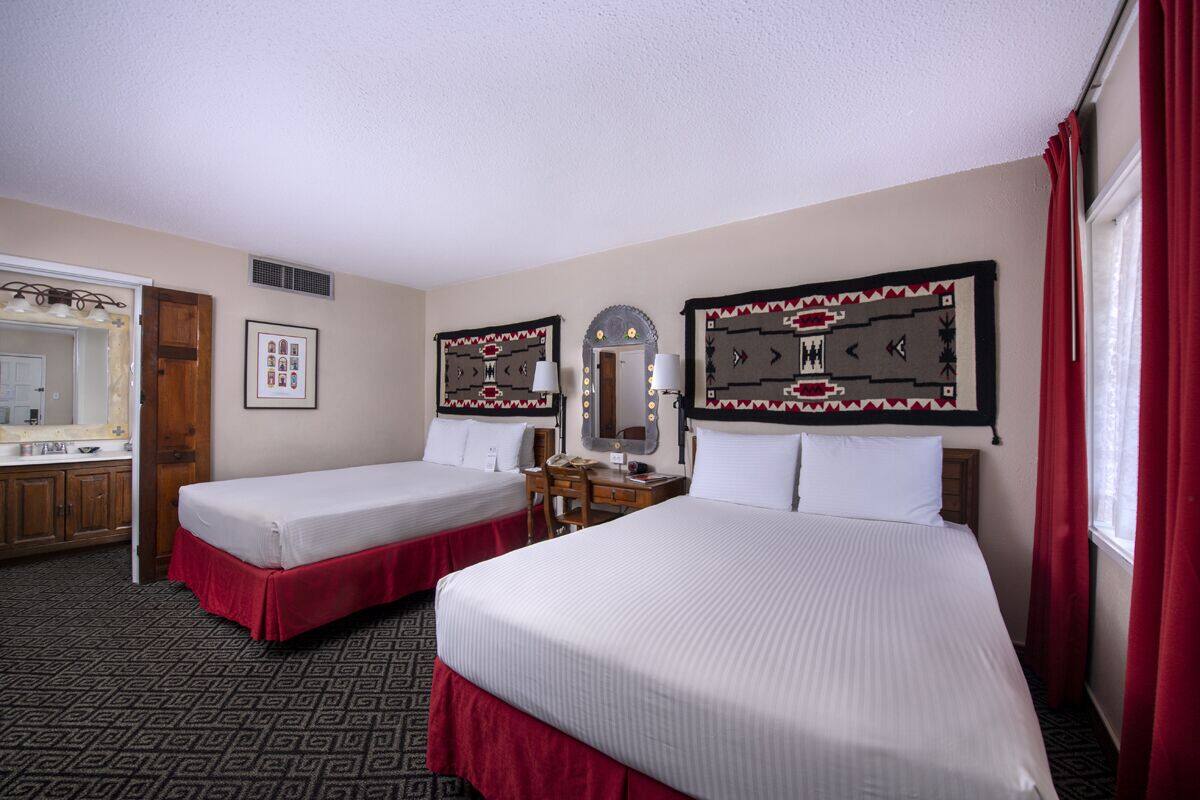 A hotel room with two single beds, a wooden desk, a mirror, and a window with red curtains.