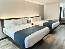 Habitación de hotel con dos camas, cada una con sábanas blancas y colchas azul marino. Hay una mesita y una silla en la habitación.