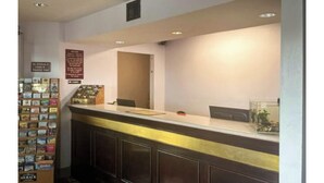 A reception area with a counter, a display of postcards, and a door leading to another room. - Studio 6 Suites Louisville, KY – Airport/Expo Center (Louisville)