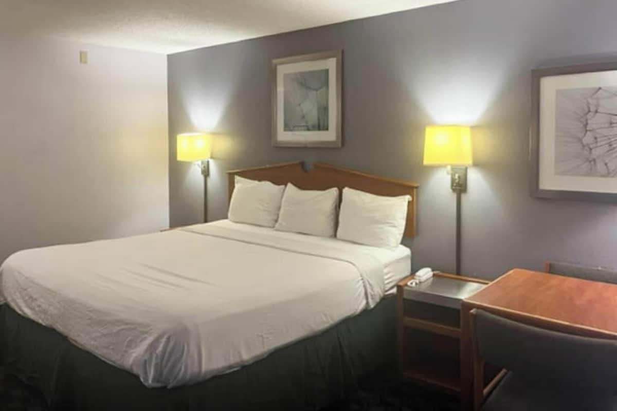 A hotel room with a large bed, two bedside lamps, a small table, and a chair.