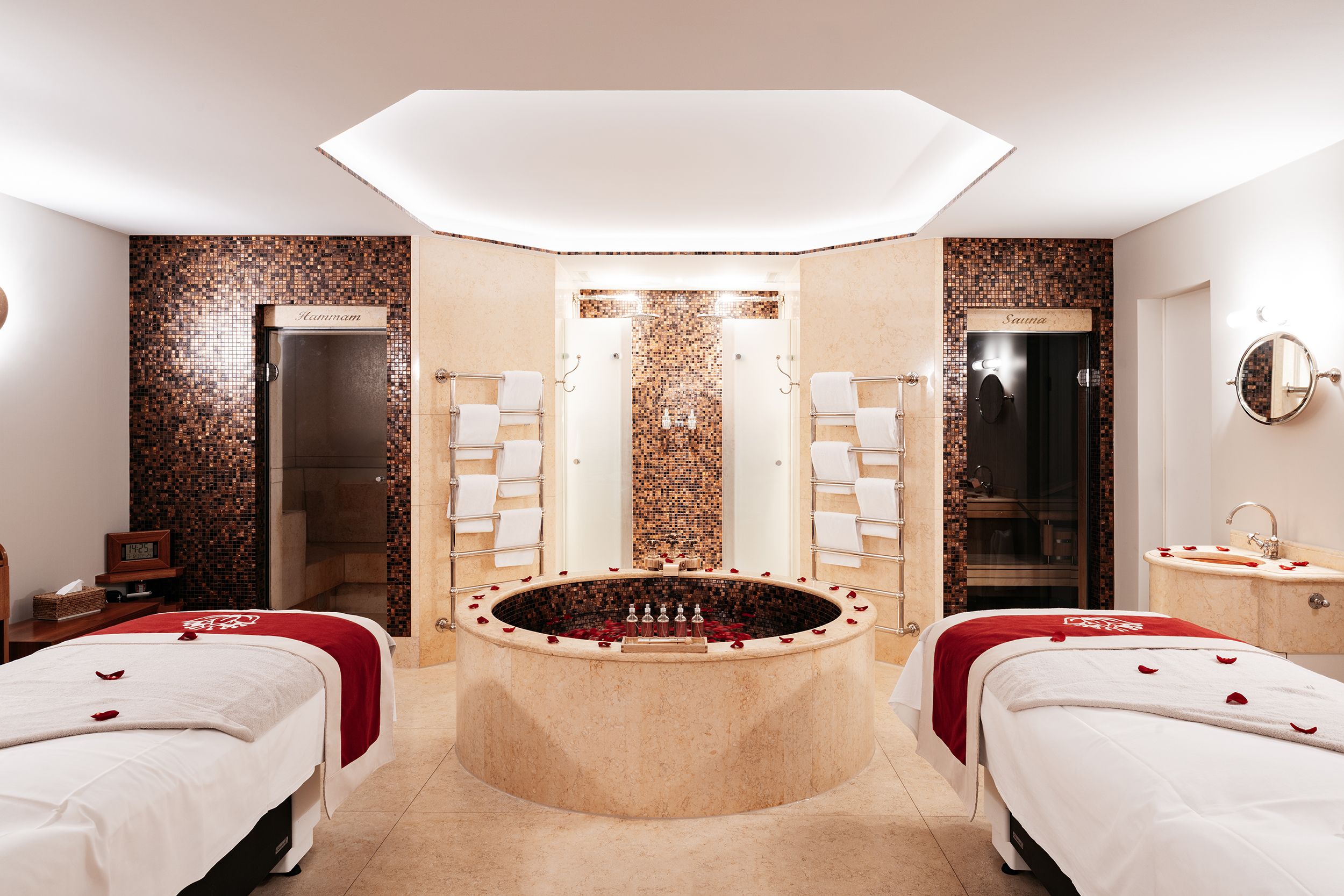 A hotel room with a central jacuzzi, two beds, a walk-in shower, and a sauna.