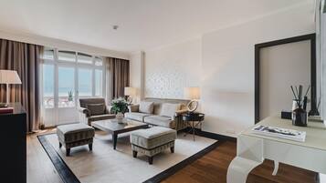 Una habitación de hotel moderna con un conjunto de sofás, una mesa de centro, un escritorio y un ventanal con cortinas.