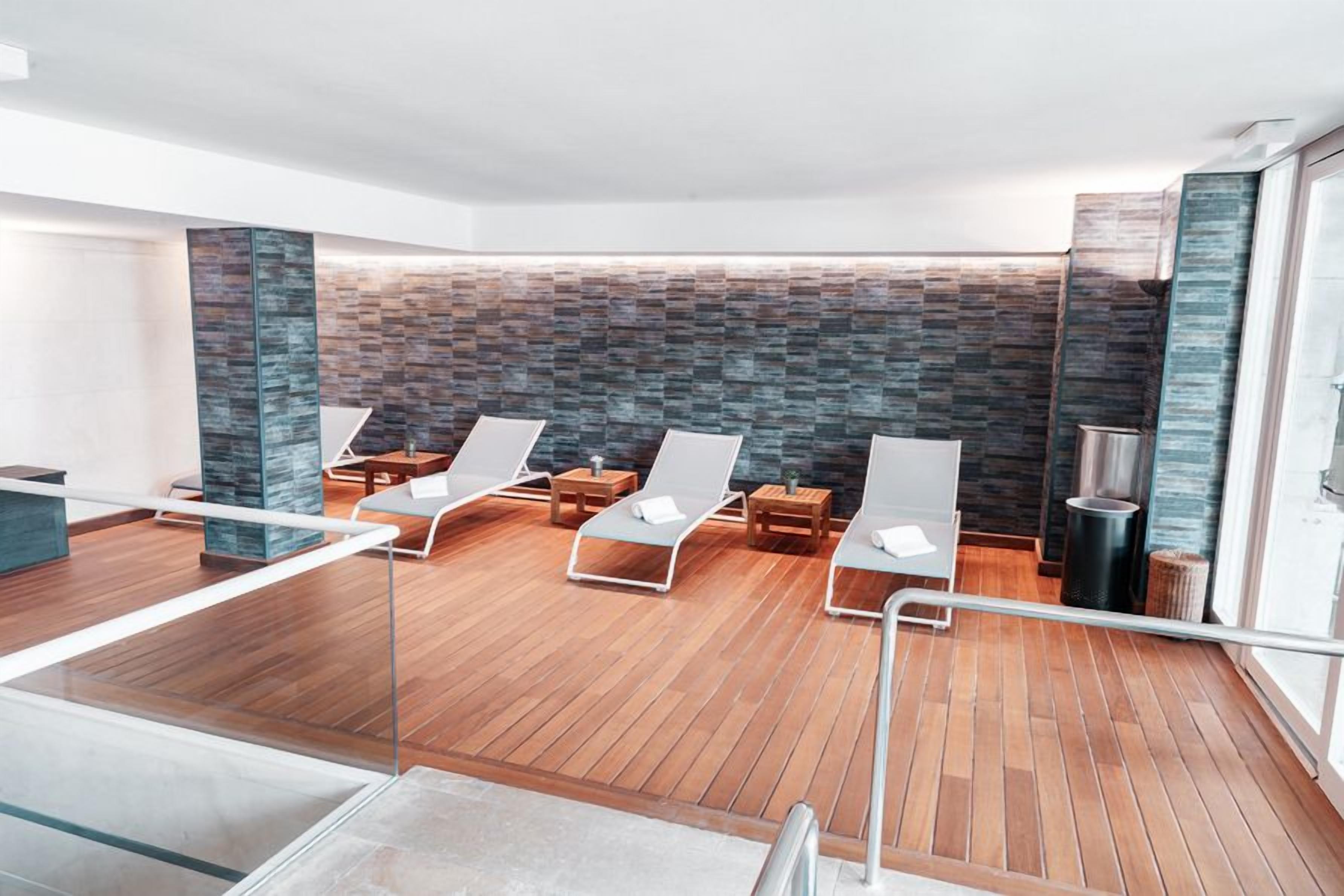 Ein moderner Wellnessbereich mit Holzboden, Liegestühlen und einer Steinwand.