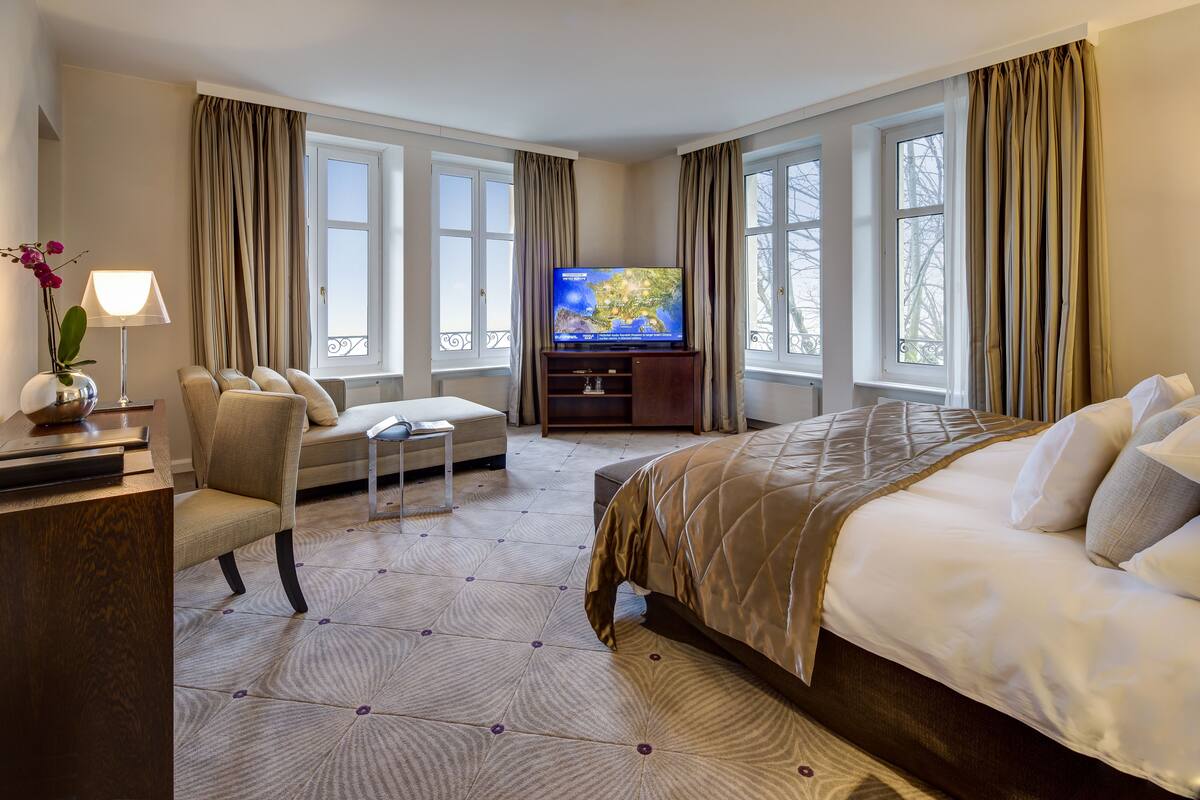Una habitación de hotel con una cama grande, un sofá, un televisor sobre un mueble de madera y un escritorio con lámpara.