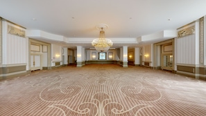 A spacious hall with a patterned carpet, a large chandelier, and wall sconces.