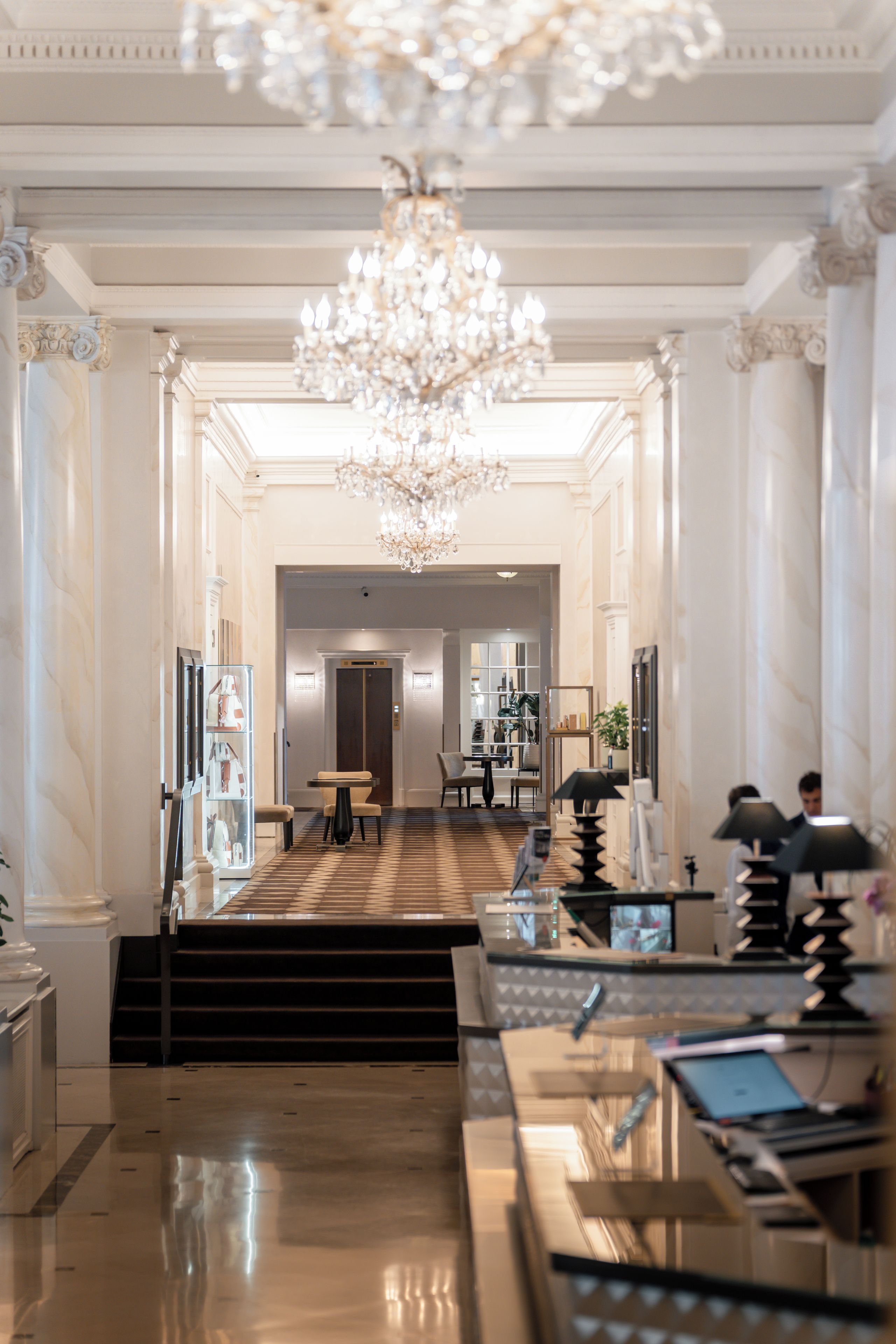 A grand lobby with a chandelier, marble columns, and a check-in counter.