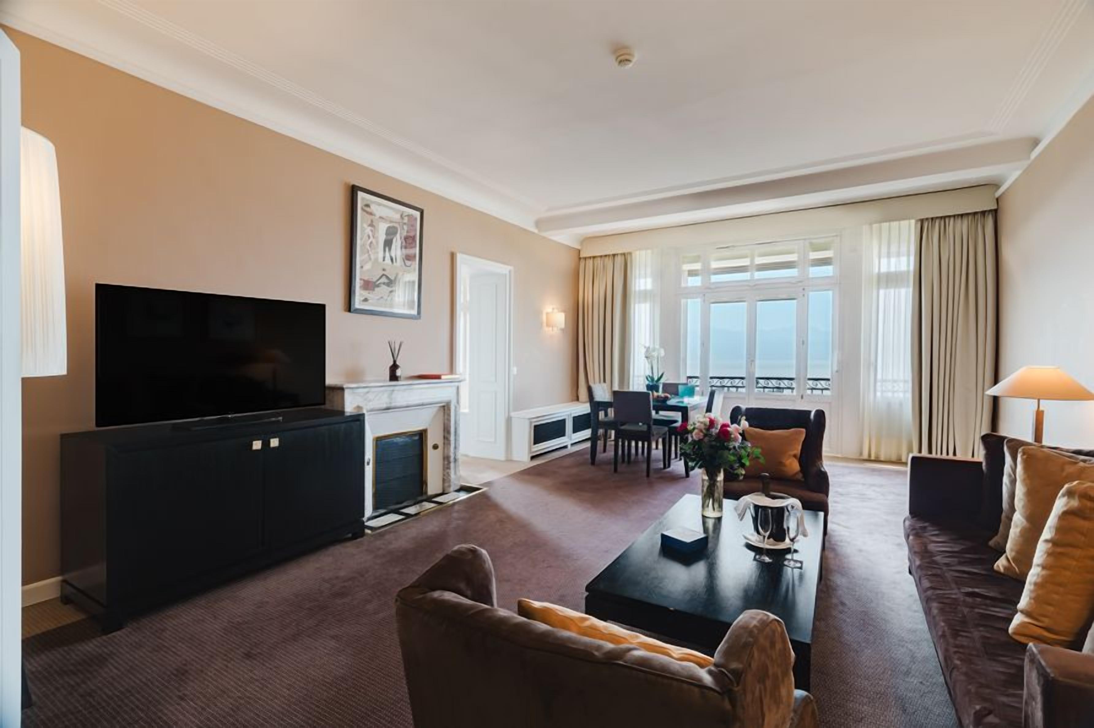 Ein Hotel-Wohnzimmer mit Flachbildfernseher, Kamin, Essbereich und Blick ins Freie.