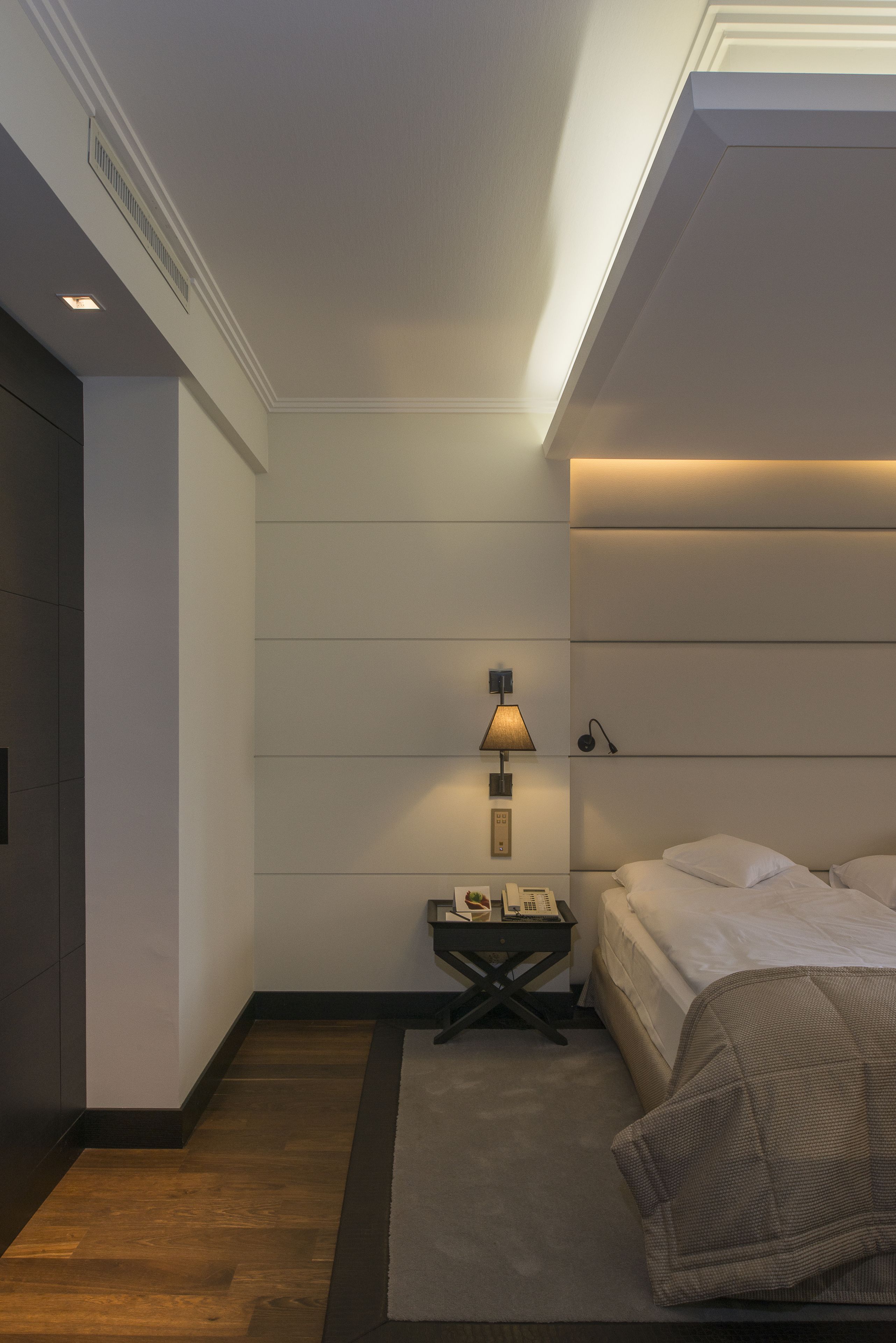Una habitación de hotel moderna con cama, mesita de noche, lámpara y una planta pequeña.