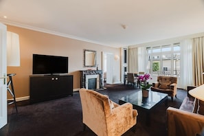 Habitación de hotel con televisión de pantalla plana, chimenea, zona de comedor y balcón con cortinas.