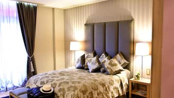 Une chambre d’hôtel bien rangée, avec un grand lit, deux tables de chevet, une valise et une petite table avec une lampe.