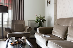 A modern living room with a sofa, armchair, and a coffee table with a tray of snacks and a coffee pot.
