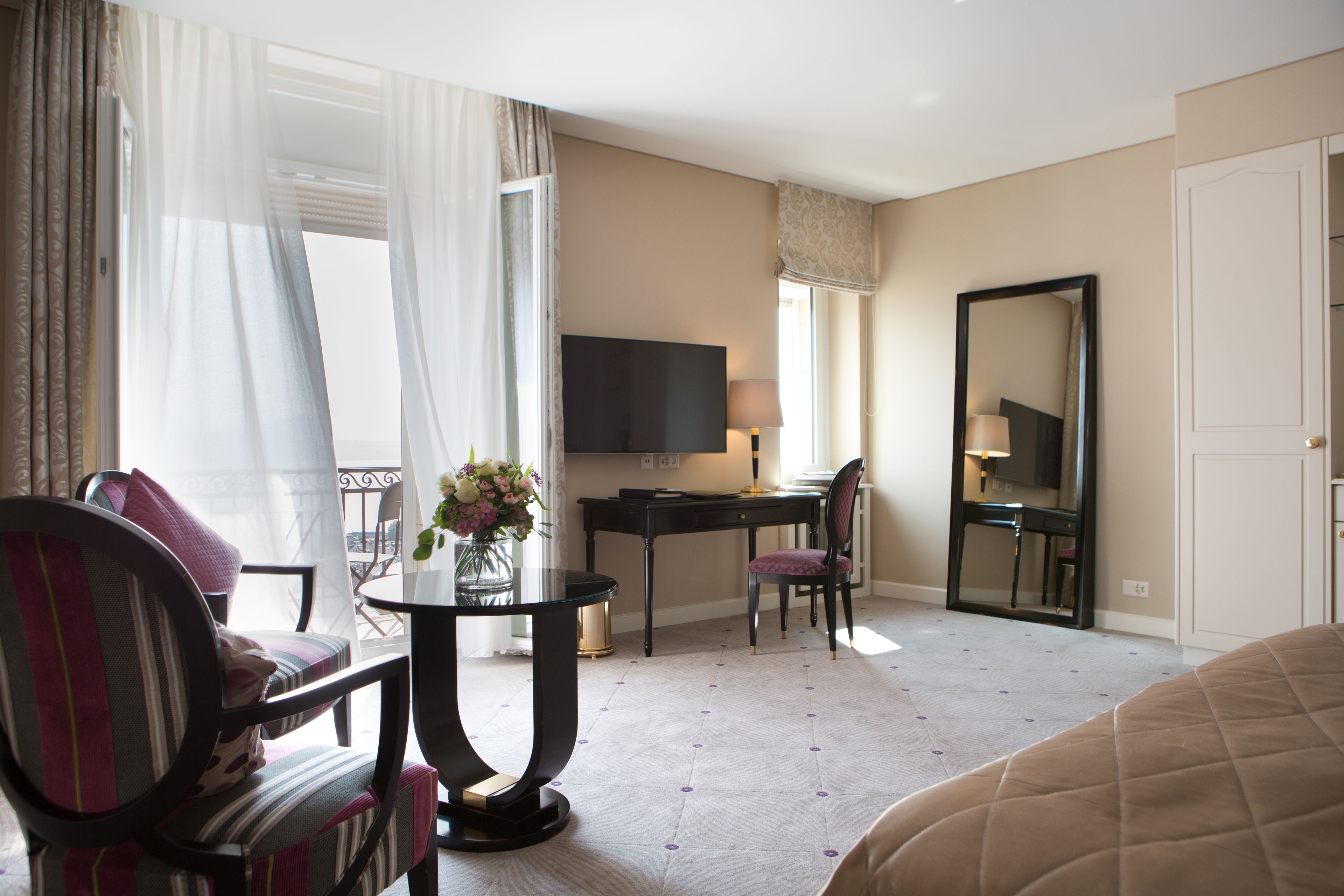 A hotel room with a bed, a desk, a chair, a TV, and a window with curtains.