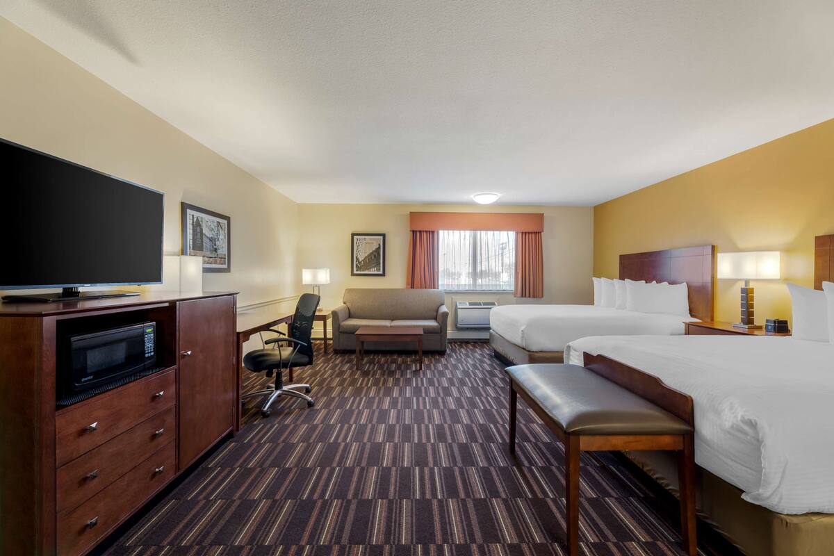 Une chambre d’hôtel équipée d’un téléviseur à écran plat, d’un canapé, d’un bureau, d’une chaise, de deux lits et d’une fenêtre avec des rideaux.
