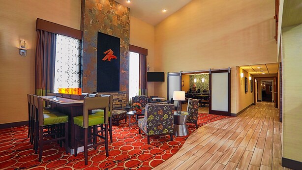 A hotel lobby with a red patterned carpet, wooden flooring, a stone accent wall, and a seating area with floral-patterned chairs and a table. - Best Western Falcon Plaza - Bowling Green (Bowling Green)